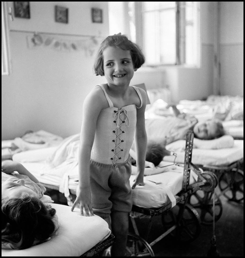 This sparkling little girl suffers from spinal tuberculosis and must wear a stiff body jacket. She was pictured, by David Seymour, in 1948 at the Bellevue Hospital, Vienna, Austria